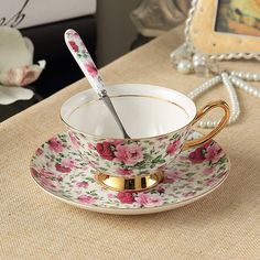 a cup with a spoon in it sitting on a table next to a flowered saucer