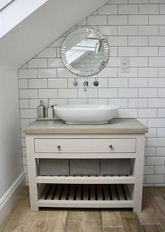 a white sink sitting under a round mirror on top of a bathroom vanity next to a wooden floor