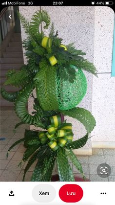 a green plant with yellow ribbons hanging from it's sides in front of a building