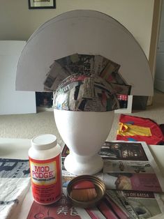 a white vase sitting on top of a table covered in magazines and other things next to it