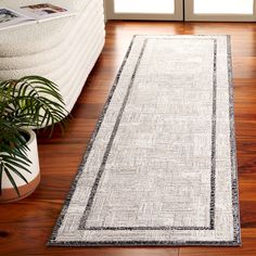 a white and black runner rug on the floor in front of a couch with potted plants