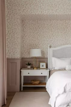 a white bed sitting in a bedroom next to a dresser and lamp on top of a wooden floor