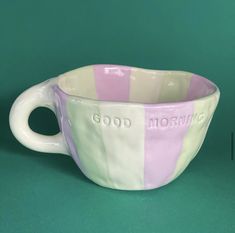 a coffee cup with the word good morning painted on it's side, sitting in front of a green background