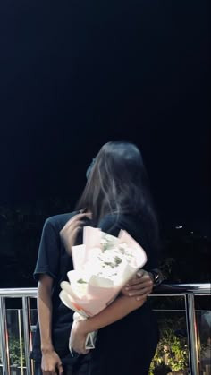 a woman is holding flowers in her hands and looking at the sky with dark background