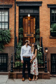 an engaged couple standing in front of a brick building