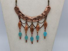 "This unique handmade statement necklace features a curved copper finish hammered bar component accented by drops created with ornate vintage copper beads, faceted copper/pink/gold crystal rondells and ending with textured turquoise magnesite stone leaves. The whole design is brought together with a subtle backdrop of copper link chain \"netting\" and is finished with custom copper lantern chains and a lobster clasp closure. This extraodinary piece comes complete with matching earrings, which me Copper Jewelry With Dangling Beads, Bronze Copper Jewelry With Dangling Beads, Bohemian Jewelry In Copper Wire With Patina, Unique Copper Jewelry With Dangling Beads, Bohemian Copper Necklace With Patina, Textured Turquoise, Diy Statement Necklace, Handmade Statement Necklace, Copper Lantern