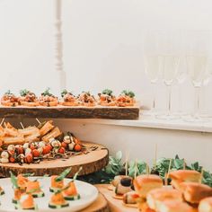 an assortment of appetizers are displayed on wooden platters with wine glasses in the background