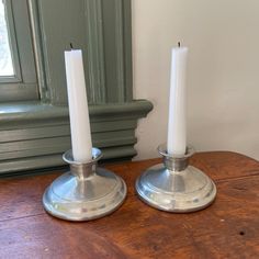 two white candles sitting on top of a wooden table