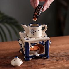 a person is pouring something into a teapot with a candle in it on a wooden table