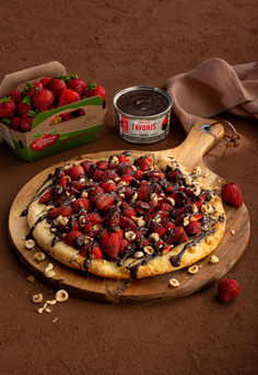 a chocolate covered pizza with strawberries and nuts next to a box of peanut butter