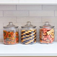 three glass canisters filled with different types of cookies and crackers on a kitchen counter