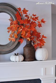 a fireplace mantel with white pumpkins and orange leaves on it in front of a mirror