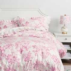 a white bed with pink flowers on it in a small room next to a lamp