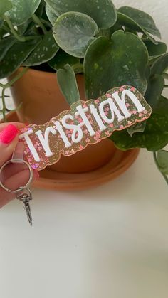 a person holding a keychain with the word kristian on it in front of a potted plant