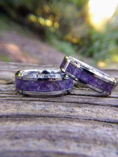 two wedding bands with amethyst purple stone inlays are sitting on a piece of wood