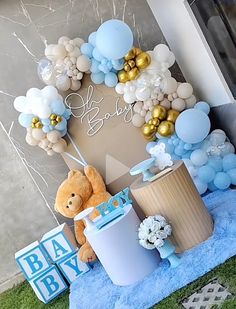 a teddy bear sitting on top of a blue blanket next to balloons and gifts in front of a door