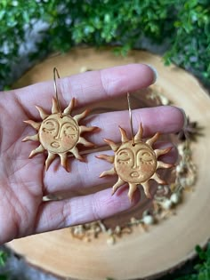 the sun and moon earrings are on someone's hand, in front of some green plants