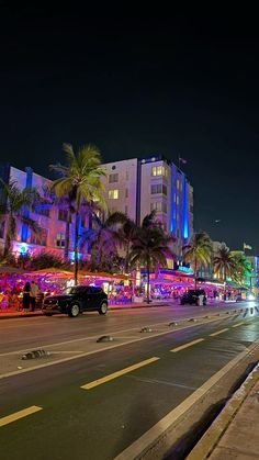 a city street at night with cars parked on the side and palm trees in the background