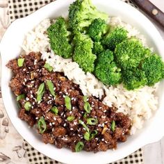 a white bowl filled with rice, meat and broccoli on top of a checkered table cloth