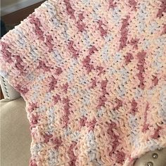 a pink and white crocheted blanket sitting on top of a chair next to a window