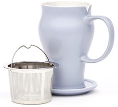 a white coffee cup next to a tea strainer and saucer on a white background