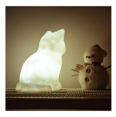 a white teddy bear sitting next to a snowman on a shelf in front of a light