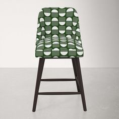 an upholstered chair with green and white designs on the back, in front of a gray wall