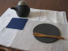 a table with a teapot, spoon and plate on it next to a napkin