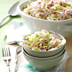 two white bowls filled with coleslaw on top of a wooden table next to silverware