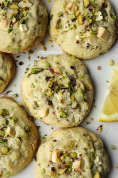 several cookies with pistachios and other toppings next to a slice of lemon