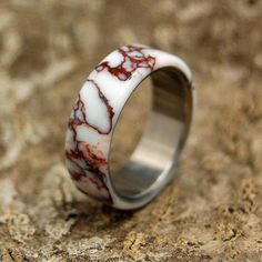 a ring with red and white marble inlays on it sitting on a rock