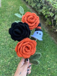 a hand holding two crocheted flowers and a small bird on top of it