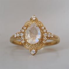 a gold ring with an oval shaped white stone surrounded by small diamonds