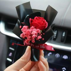 a person is holding a red rose in their hand and it's ribbon around the car steering wheel