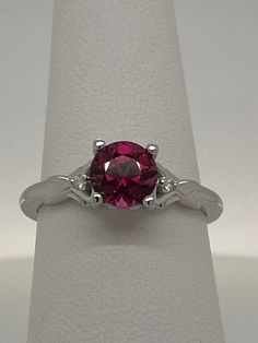 This natural round Rhodolite Garnet is 1.45ct purplish red and set in a 14K white gold ring size 7 (sizable) with .02ctw VS G-H Diamond Melee.  Each side of the ring as a heart-shape with a 1.4mm diamond set inside.  The name Rhodolite is derived from the Greek "rhodon" for "rose-like".  This stone has great color, cut and clarity. Garnet is the birthstone for the month of January. I am a GIA Graduate Gemologist with a passion for all gemstones.  I have a 30 day return policy so if do not wish to keep this item, simply return to me for your refund. Clarity        Eye-Clean Carat Weight1.45 carats Shape         Round Cut                Step Cut Enhancement (N) None  Gemstone Enhancement Codes*  N = Not Enhanced B = Bleaching C = Coating  D = Dyeing F = Filling H = Heating  HP = Heat & Press 14k White Gold Ruby Ring With Brilliant Cut, Lab-created Ruby Diamond Ring With Prong Setting, Garnet Birthstone Ring With Prong Setting, Red Round Solitaire Sapphire Ring, Red Solitaire Sapphire Ring, 14k White Gold Ruby Ring With Center Stone, Classic White Gold Ruby Ring With Round Stone, 14k White Gold Round Ruby Ring With Center Stone, White Gold Ruby Ring With Center Stone