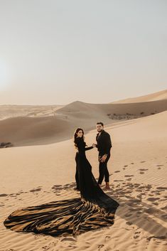 a man and woman standing on top of a sandy beach next to each other in the desert