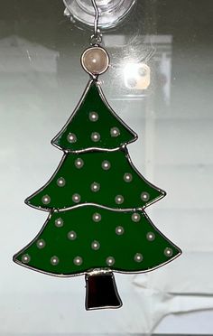 a green christmas tree shaped glass ornament hanging from a hook on a window