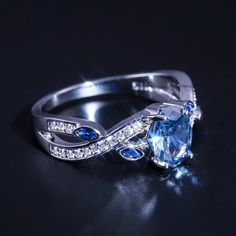 a blue and white diamond ring sitting on top of a black surface with diamonds around it