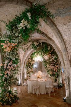 an indoor wedding with flowers and greenery on the walls, tables set up for a formal dinner