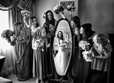 a group of women standing next to each other in front of a mirror holding bouquets