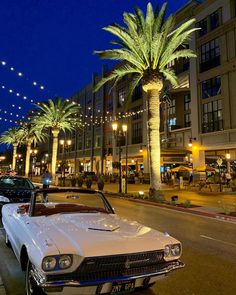 a white car parked on the side of a road next to palm trees and buildings