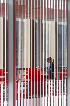 a woman sitting at a table in front of a window with vertical blinds on it