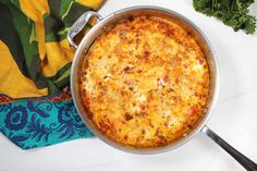 a casserole dish with cheese and vegetables on a table next to a towel