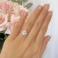 a woman's hand with a diamond ring on it and roses in the background