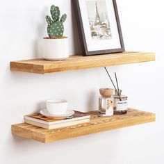 two wooden shelves with books, coffee cups and a cactus on one shelf in the corner