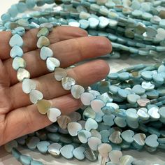 a hand is holding several pieces of blue and white agate glass beads with hearts on them