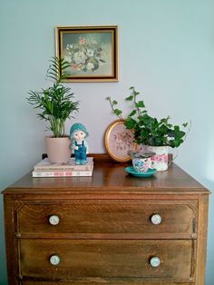 a wooden dresser topped with potted plants next to a framed picture on the wall