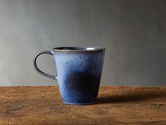 a blue coffee cup sitting on top of a wooden table next to a gray wall