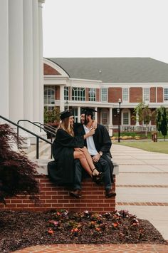 a man and woman sitting on top of a brick wall next to a white building