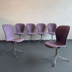 six purple chairs lined up against a white wall in a room with grey flooring